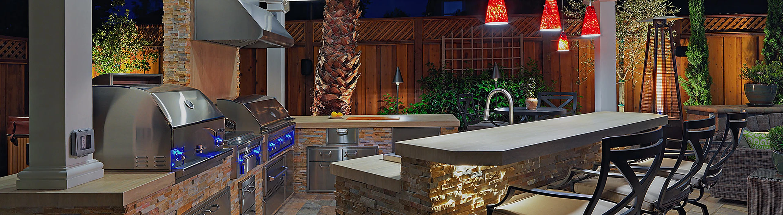 Custom outdoor kitchen suite with stainless steel grill and illuminated stone bar