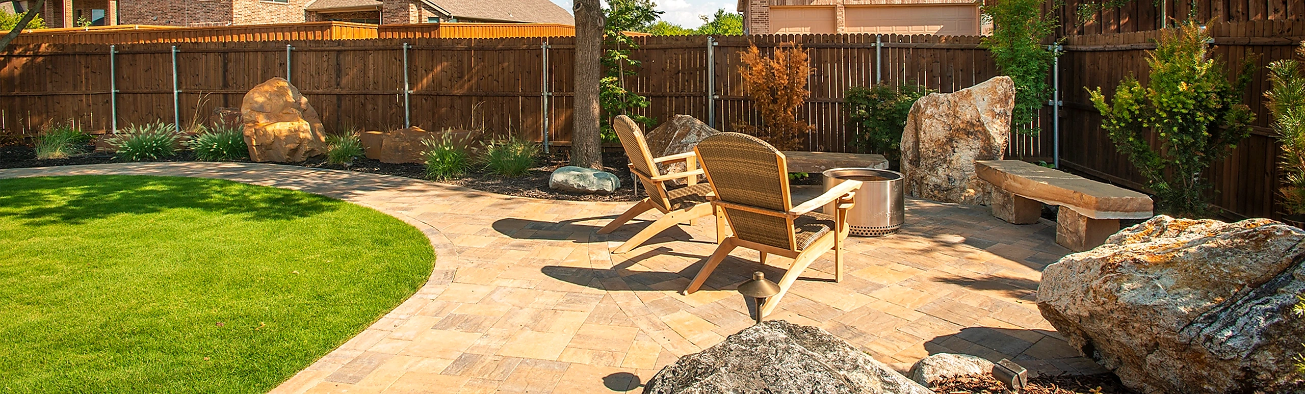 Spacious curved backyard patio paver installation with fire pit and stone seating