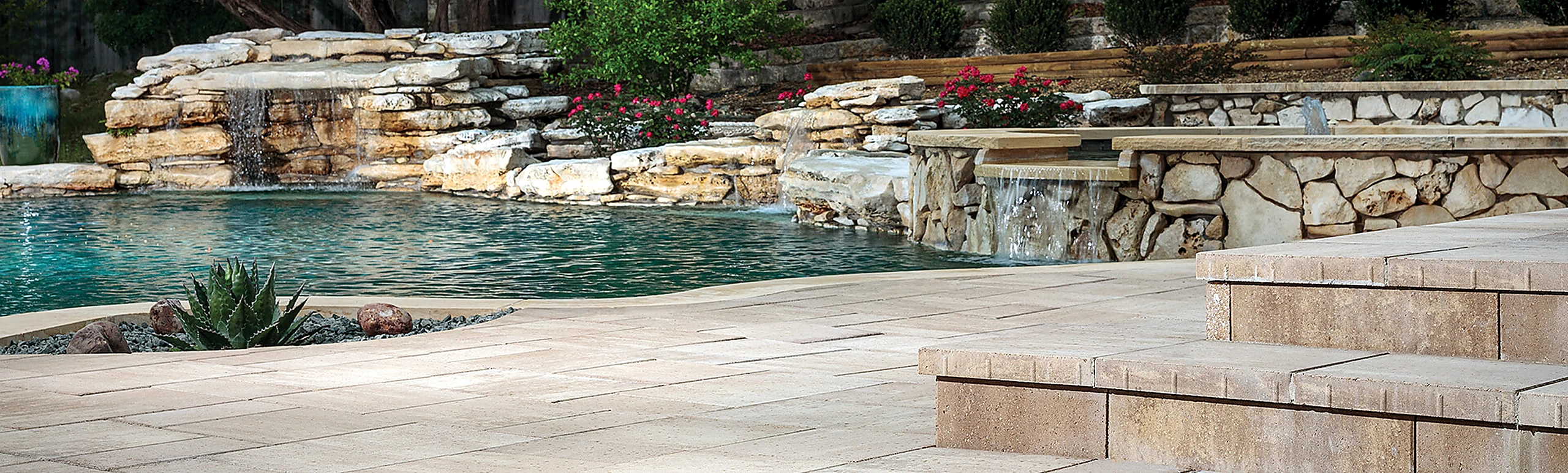Luxury swimming pool surrounded by cool-touch non-slip stone pavers and natural waterfalls